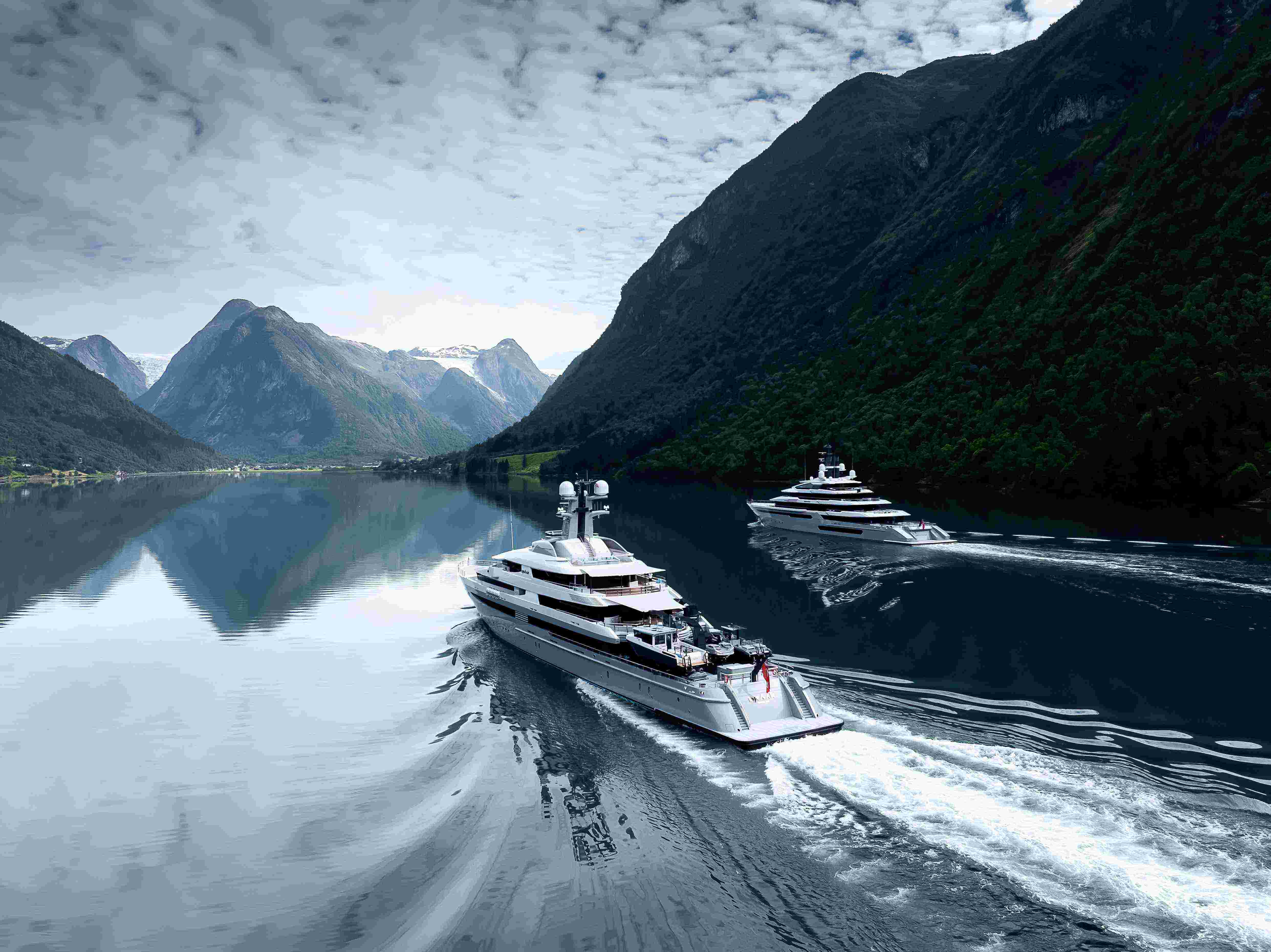 Two superyachts cruising in calm waters in a fjord