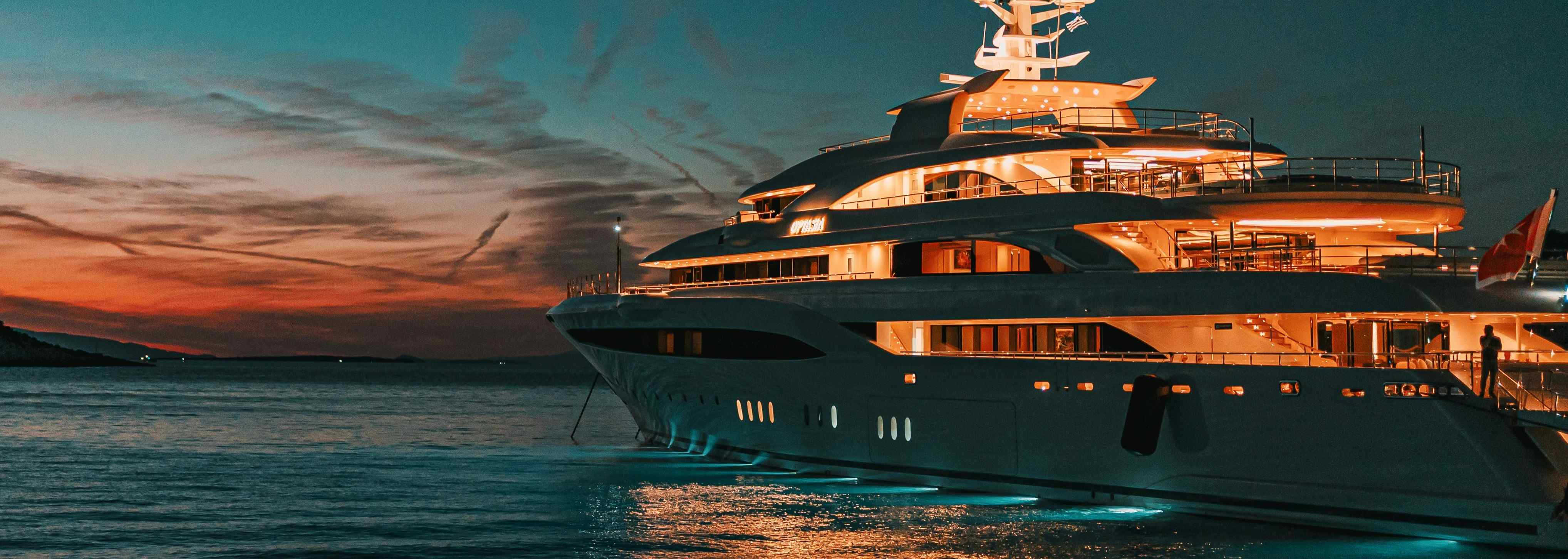 A superyacht at dusk illuminated by its interior lights