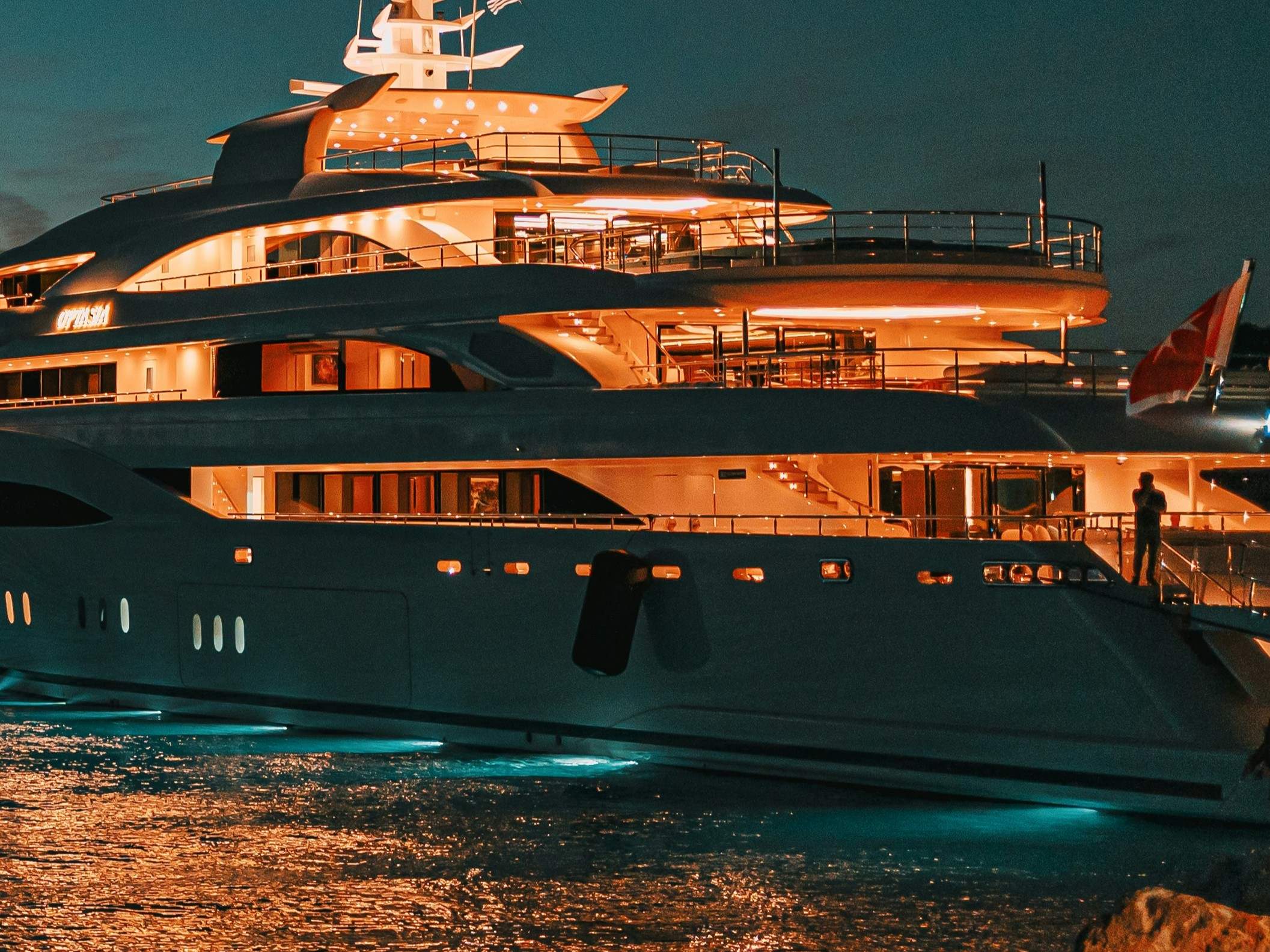 A superyacht at dusk illuminated by its interior lights