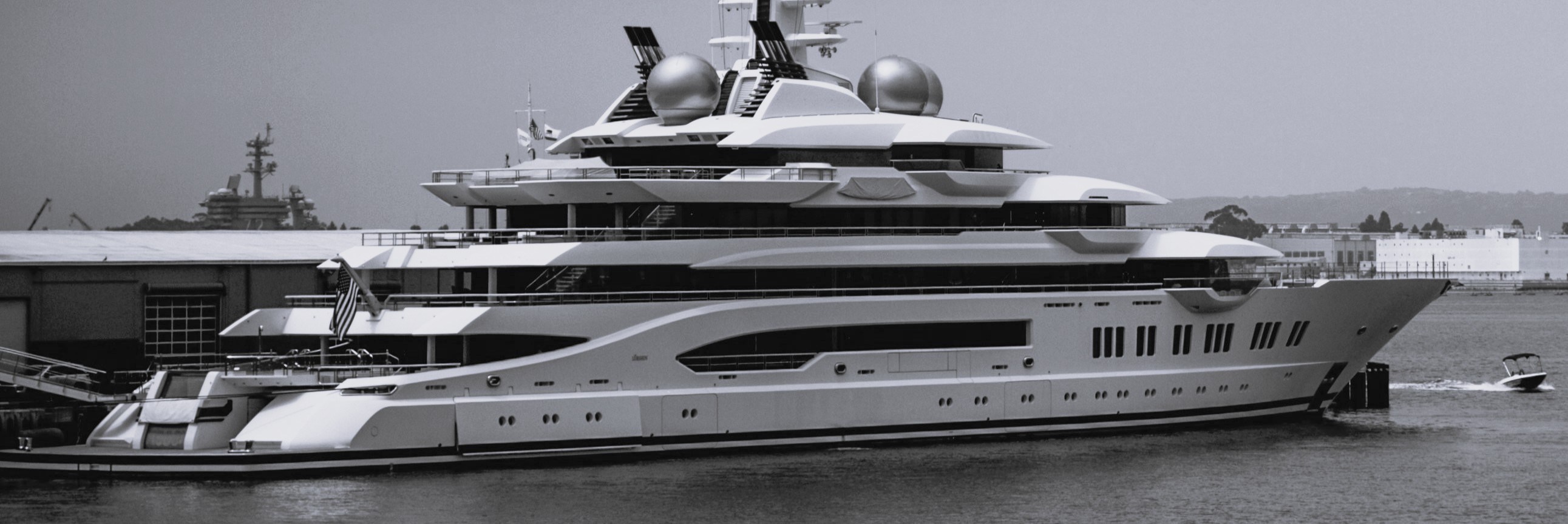 A black-and-white image shows a very large modern superyacht at dock