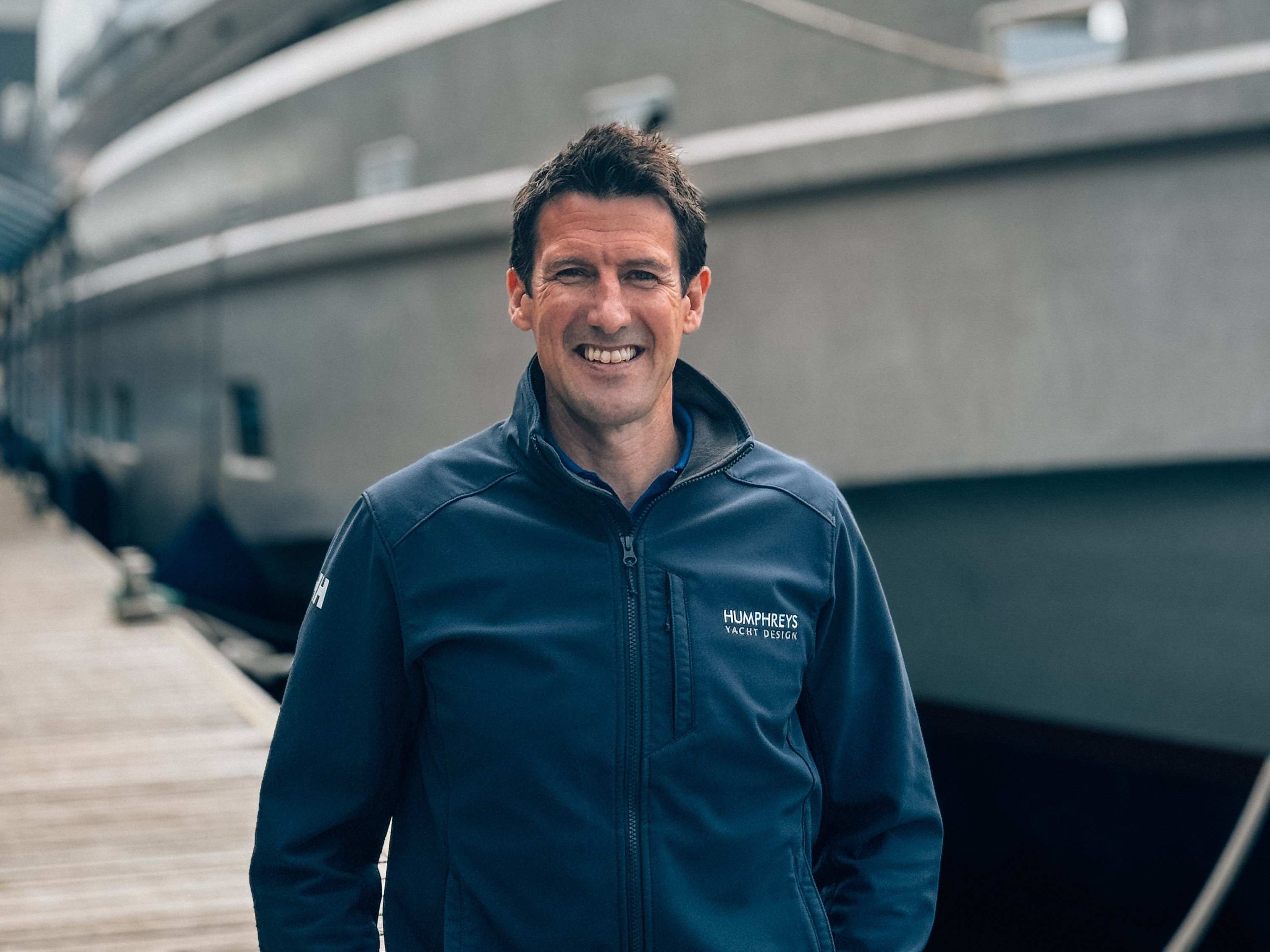 A profile photo of Tom Humphreys standing in front of a docked yacht